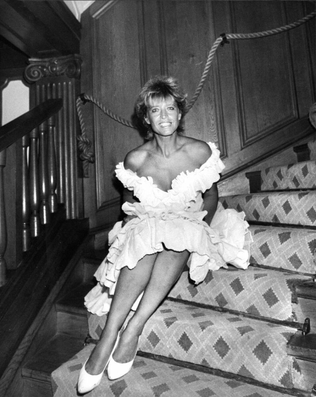Lill-Babs sitter i en trappa 1988 och ler i en vit klänning med bara axlar.