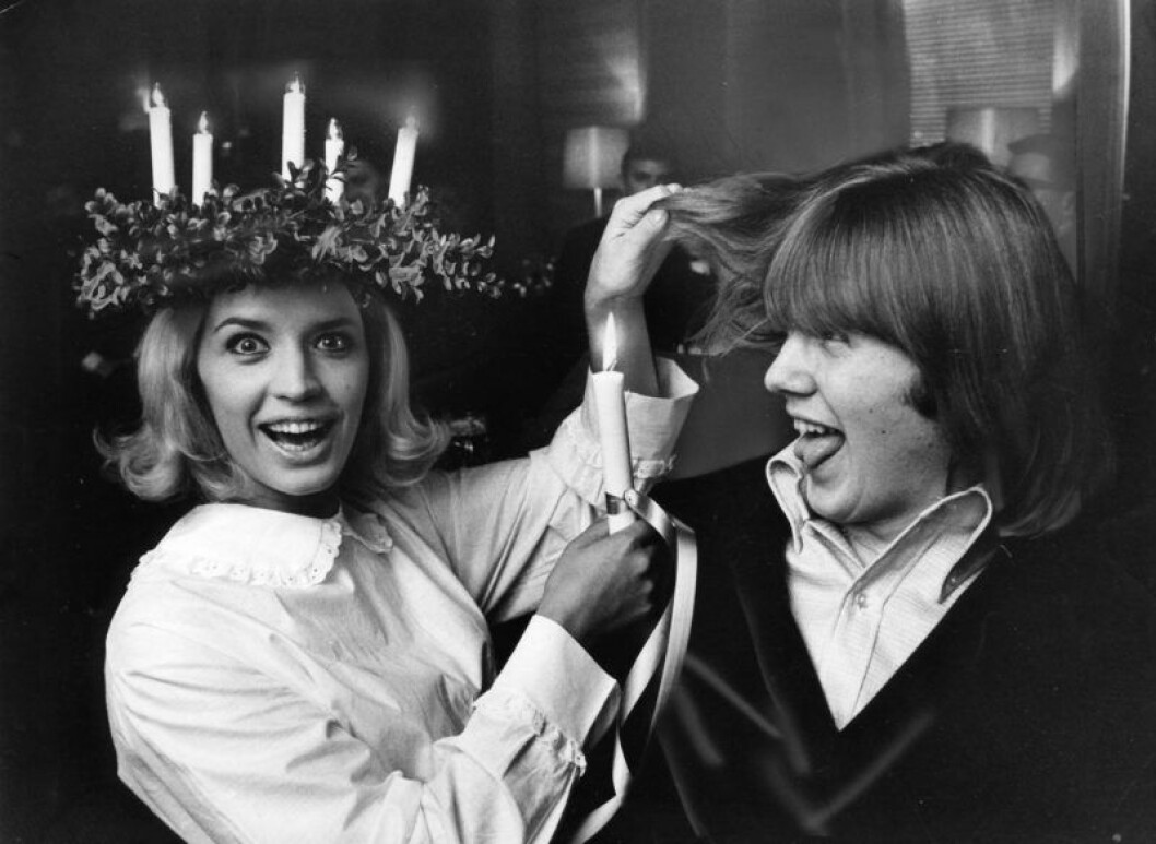 Lill-Babs med lucialinne och luciakrona och en ljus i handen, som hon skämtsamt håller nära Benny Anderssons hår.
