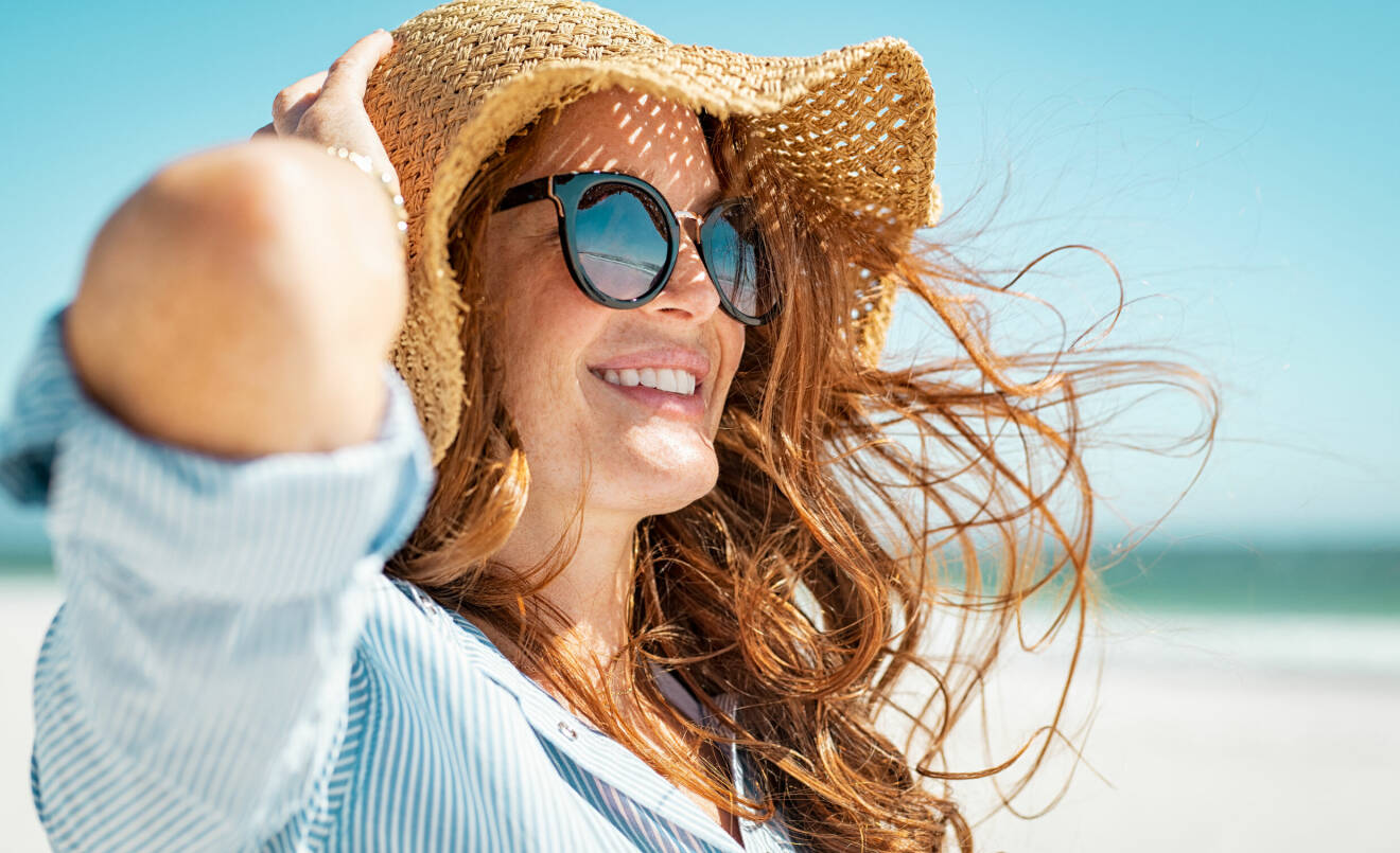 En kvinna i hatt och solglasögon på stranden