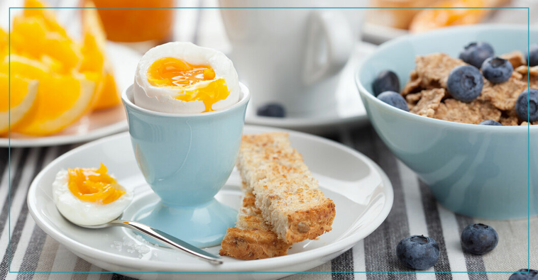 Frukost med ett löskokt ägg, bröd, blåbär, flingor och apelsin.