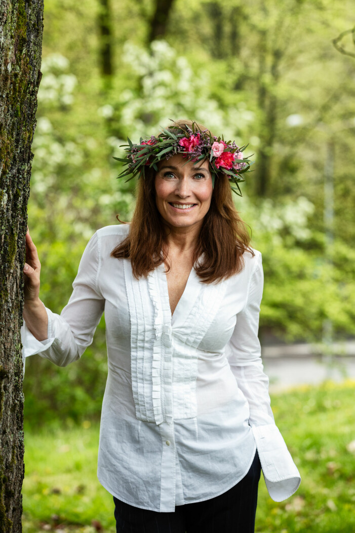 Agneta Sjödin kröntes i sin krans inför <em>Sommar</em> i P1 2021. agneta sjödin i vit skjorta, vid ett träd i en krans med röda och vita blommor.