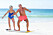 Ett äldre par, en man och en kvinna, står på en surfingbräda på en strand.
