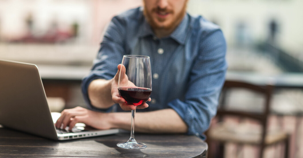 Man sitter framför sitt bord på en servering och sträcker sig efter ett glas med vin
