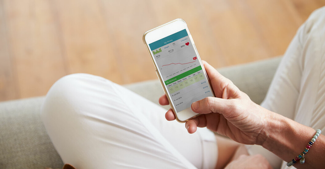 Kvinna sitter och tittar i en hälsoapp i sin mobil