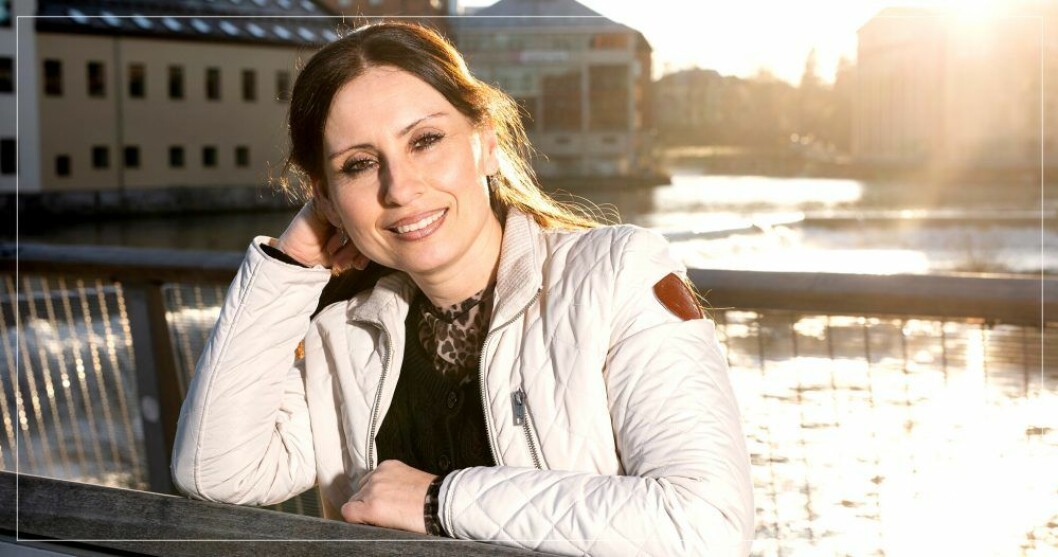 – Jag är inte rädd för honom längre. Jag är mest arg, säger Ayse Johansson. Kvinna i ljus jacka lutar armen mot ett broräcke och ler i solen