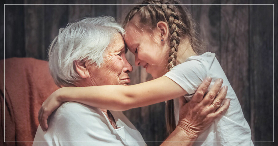 gammal kvinna med vitt hår kramar sitt barnbarn som har flätor i håret