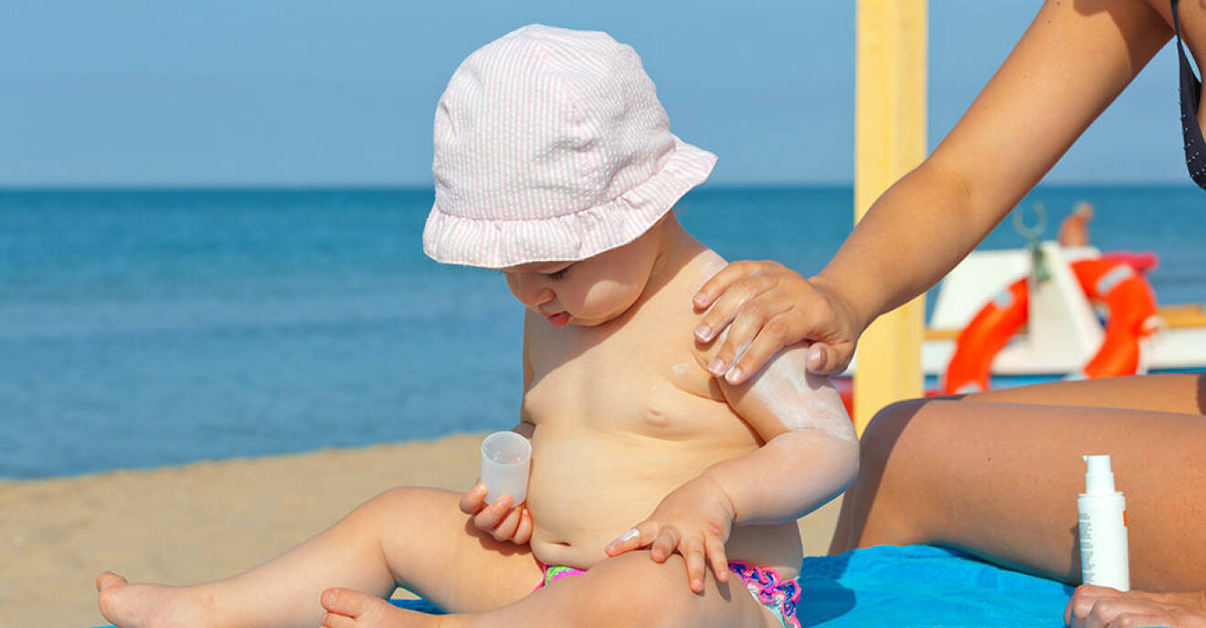 Mom puts sunscreen on the shoulders of her one year old daughter.