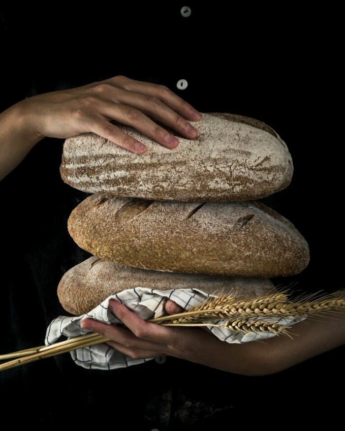 Person håller i tre nybakta limpor bröd