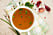 En skål med buljong på en kökshandduk. Bredvid ligger ett par vitlöksklyftor, persilja och gräslök.