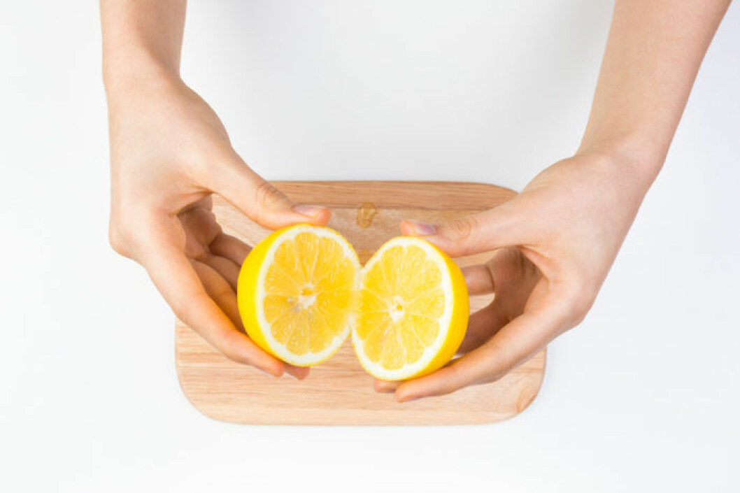 Bild: Shutterstock/IBL Ett par kvinnohänder håller en delad citron ovanför en träskärbräda.