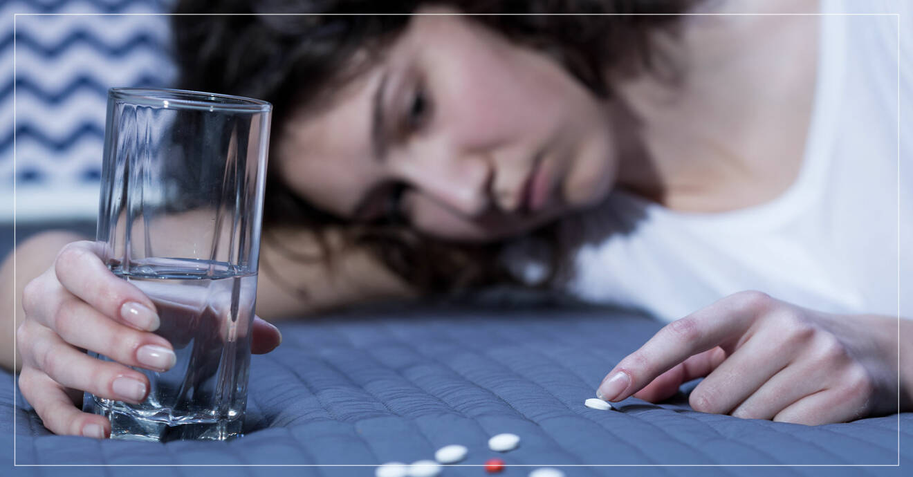 Deprimerad kvinna ligger i sängen med en hög piller