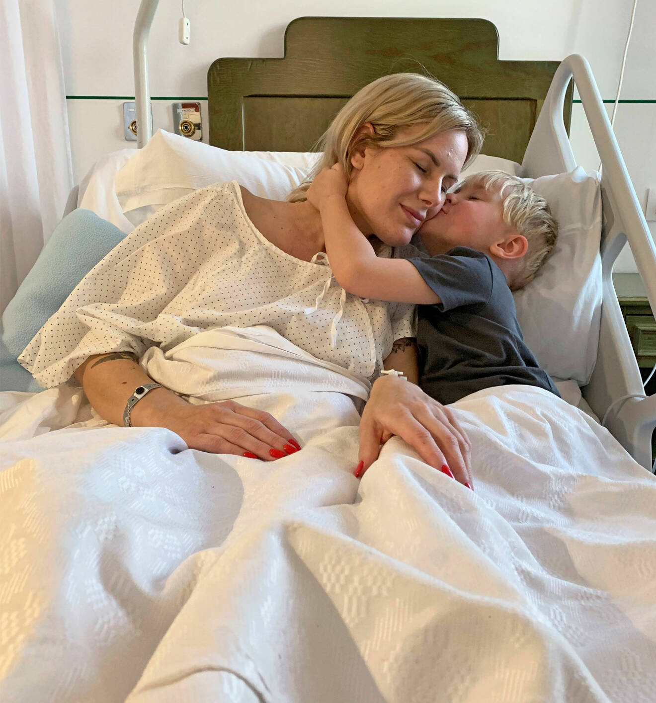Elin ligger i en sjukhussäng och får en puss av sin lille son.