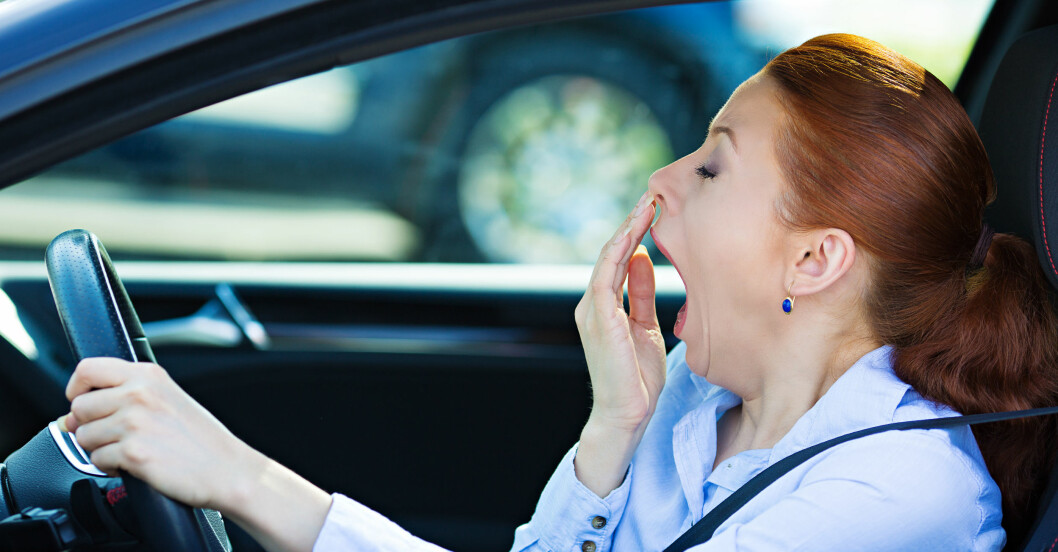 Kvinna kör bil och gäspar stort av trötthet.