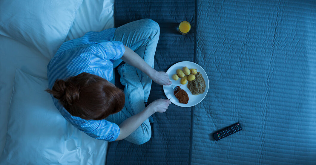 Kvinna i pyjamas sitter och äter mat i sängen på kvällen