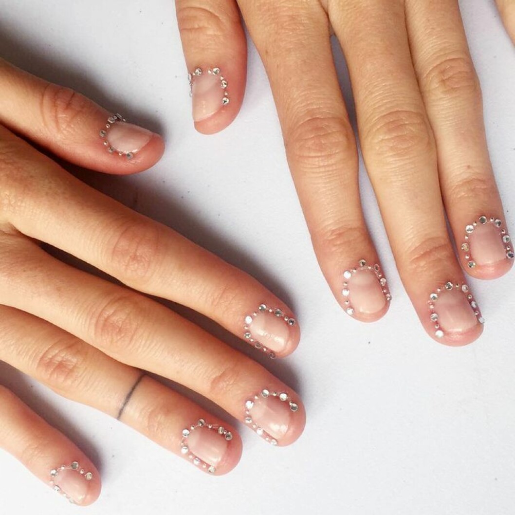 En bild på en skimrande manikyr med glittrande stenar runt nageln. 