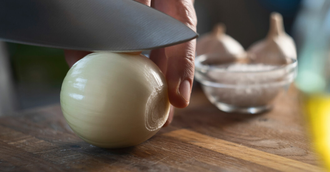 När man delar löken på mitten bör man göra det på denna ledden. En kniv som skär genom en lök.