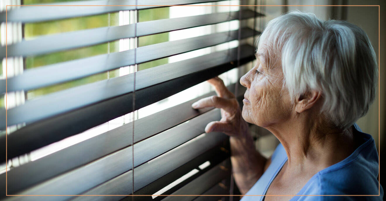 Äldre kvinna glipar på persiennen och tittar ut genom fönstret