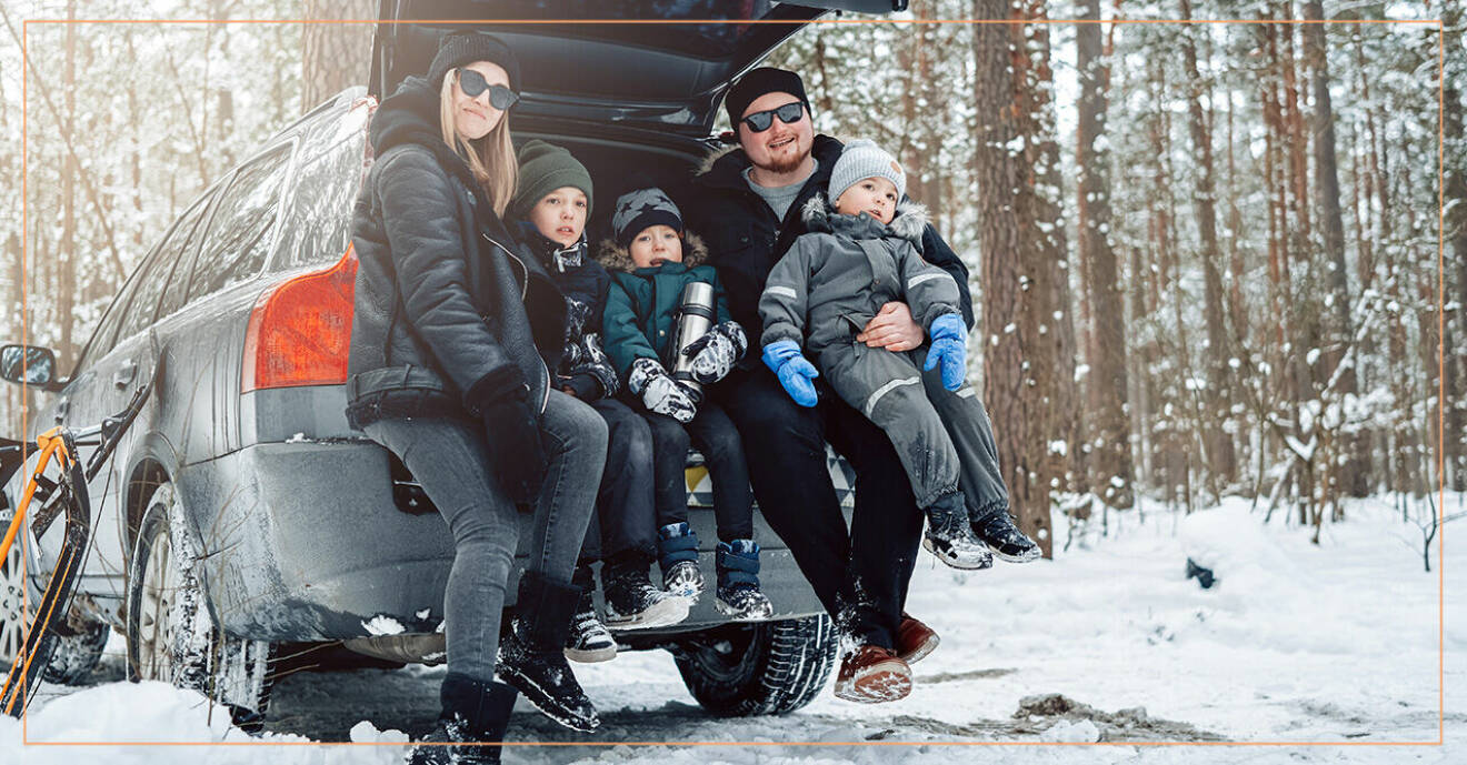 Mamma, pappa och tre barn sitter i bagageutrymmet på sin bil en snöig vinterdag