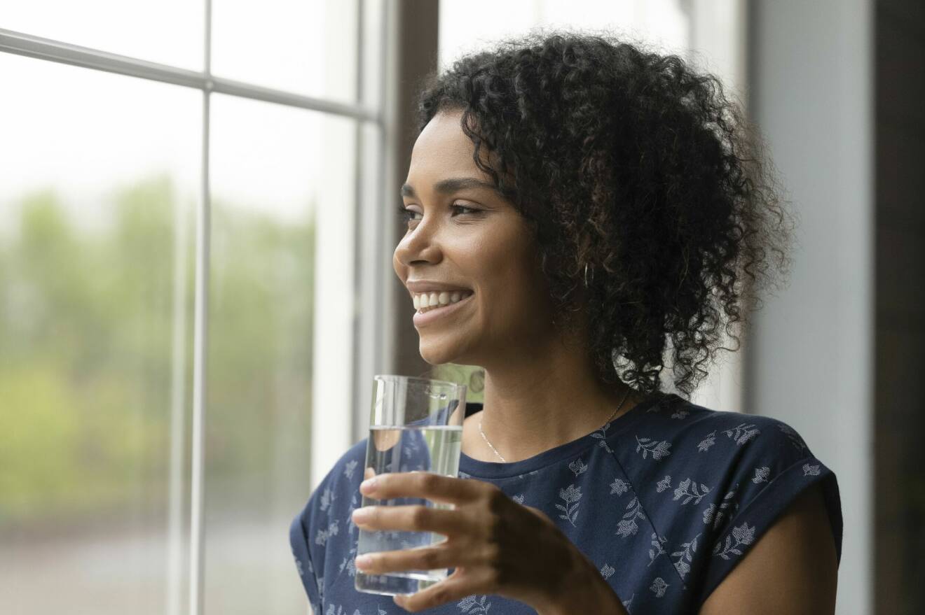En kvinna som tittar ut genom ett fönster och dricker vatten.