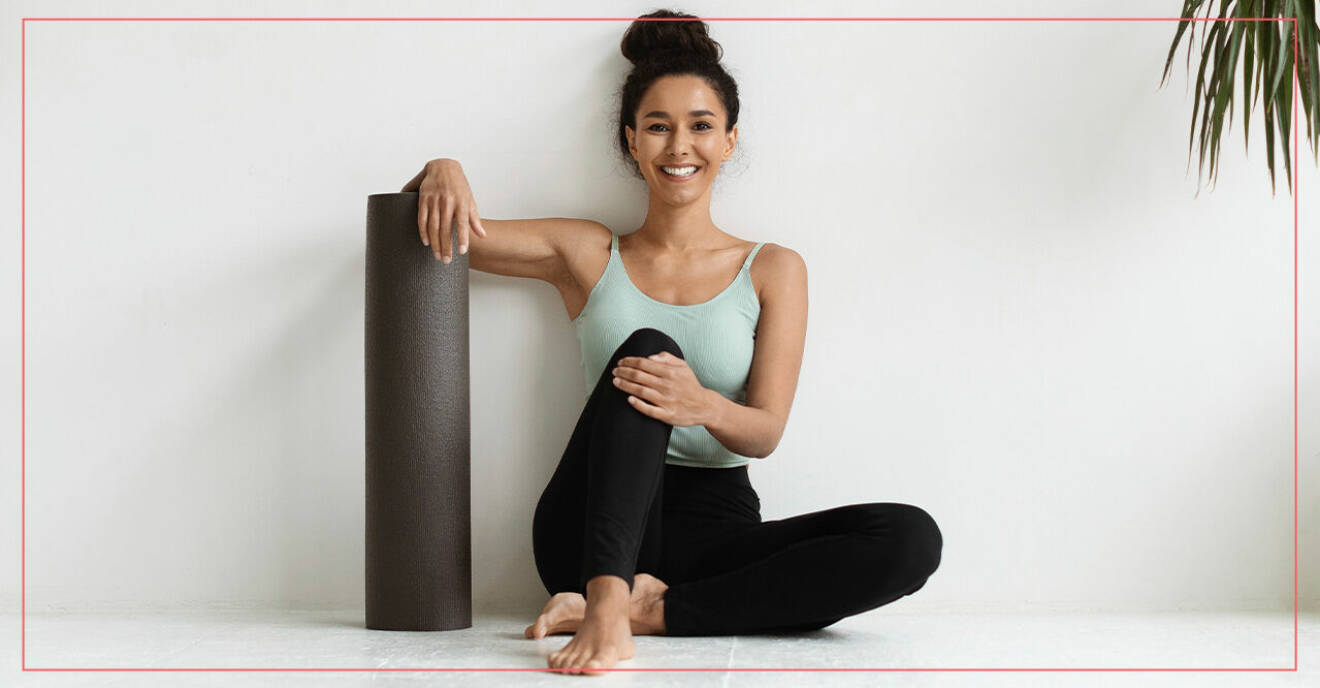 En kvinna med en yogamatta som sitter mot en vägg.