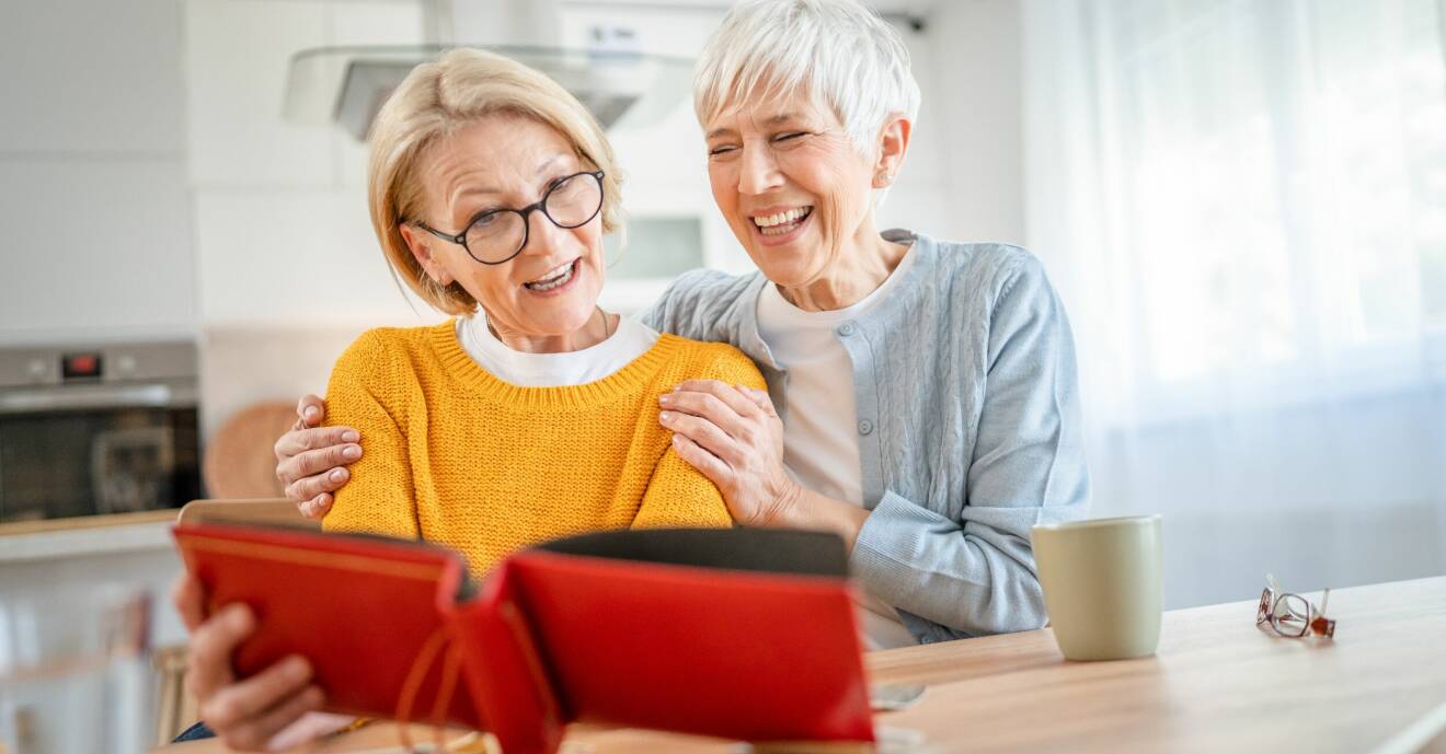 Två äldre kvinnor skrattar och tittar i fotoalbum