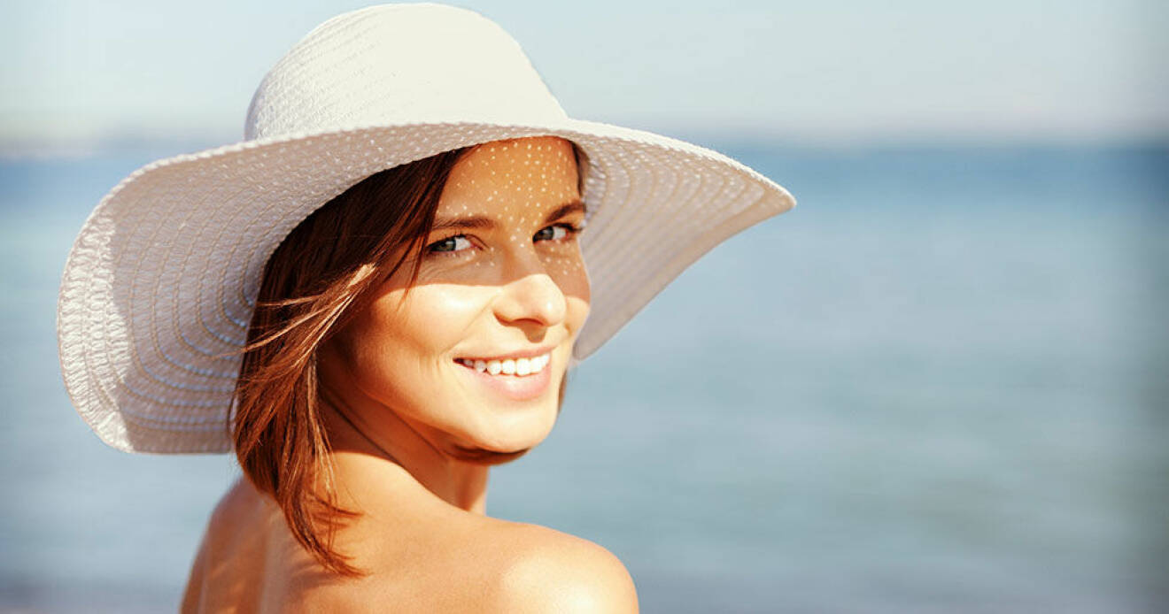 En kvinna i hatt solar sig på stranden. Under sommarhalvåret får vi D-vitamin från solen. 