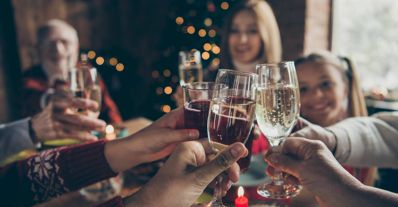 Familj med gamla och barn sitter vid dukat bord och skålar i alkohol och vatten under julfirandet.