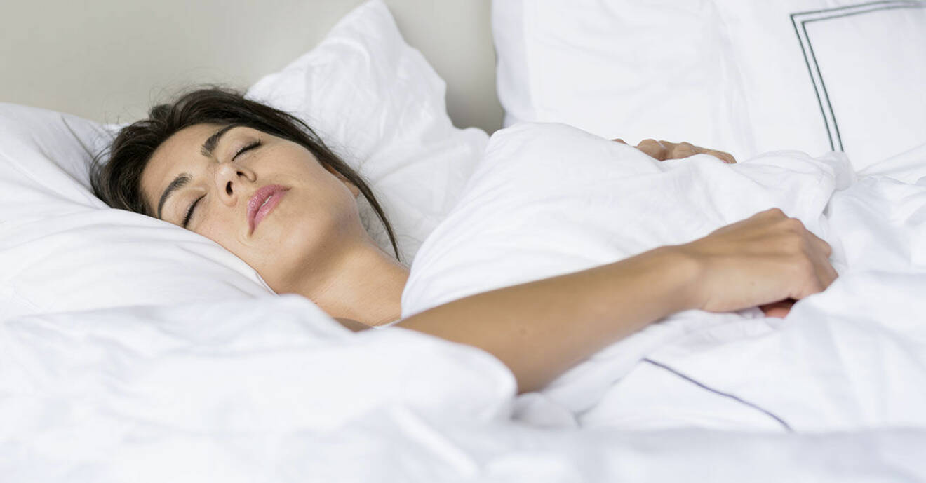 Kvinna sover på rygg i säng med vita sängkläder