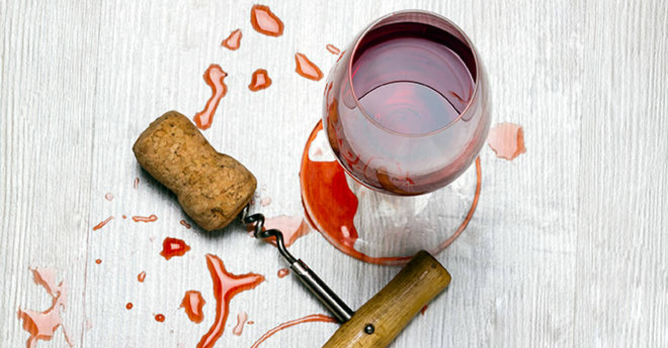 Glas med rött vin och vinskruv på ett vinfläckigt bord.