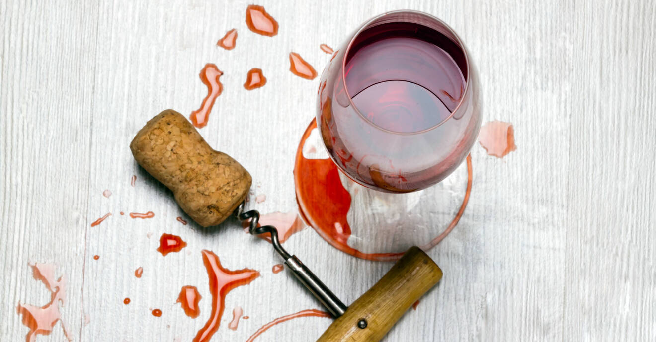Glas med rödvin och en korkskruv med kork står på bord där rödvin har spillts ut.