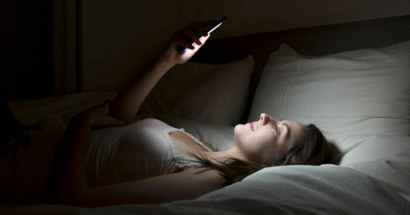 Kvinna med smartphone i sängen