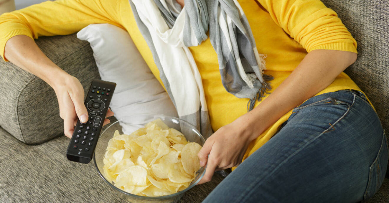 Kvinna i tv-soffa med fjärrkontroll och chips