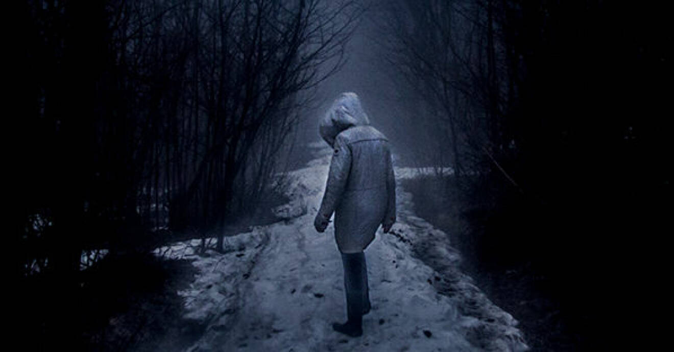 Kvinna i jacka med huva på snöig stig i skogen i mörkret