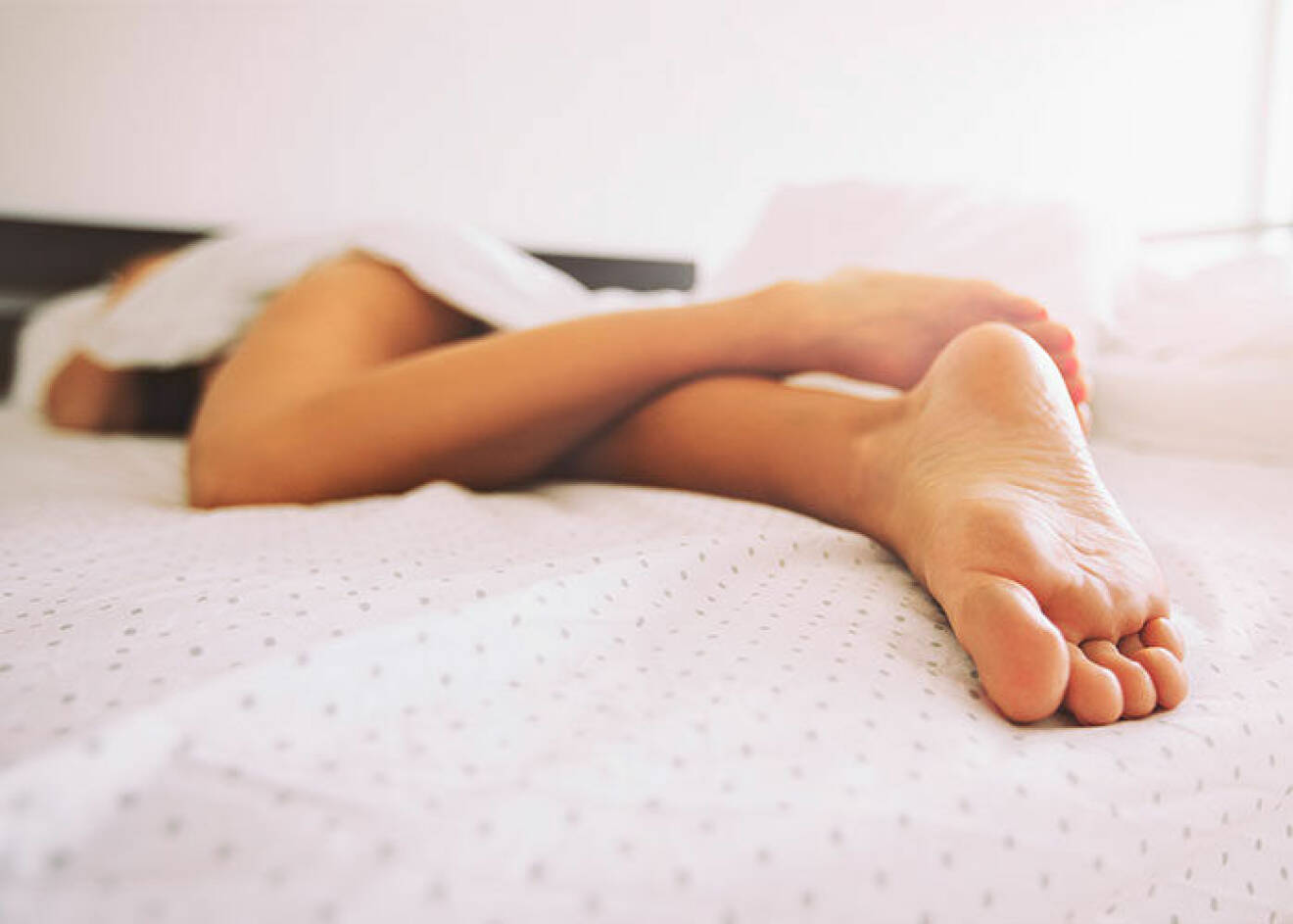 Kvinna som ligger i sängen och har ont på grund av sjukdomen restless legs