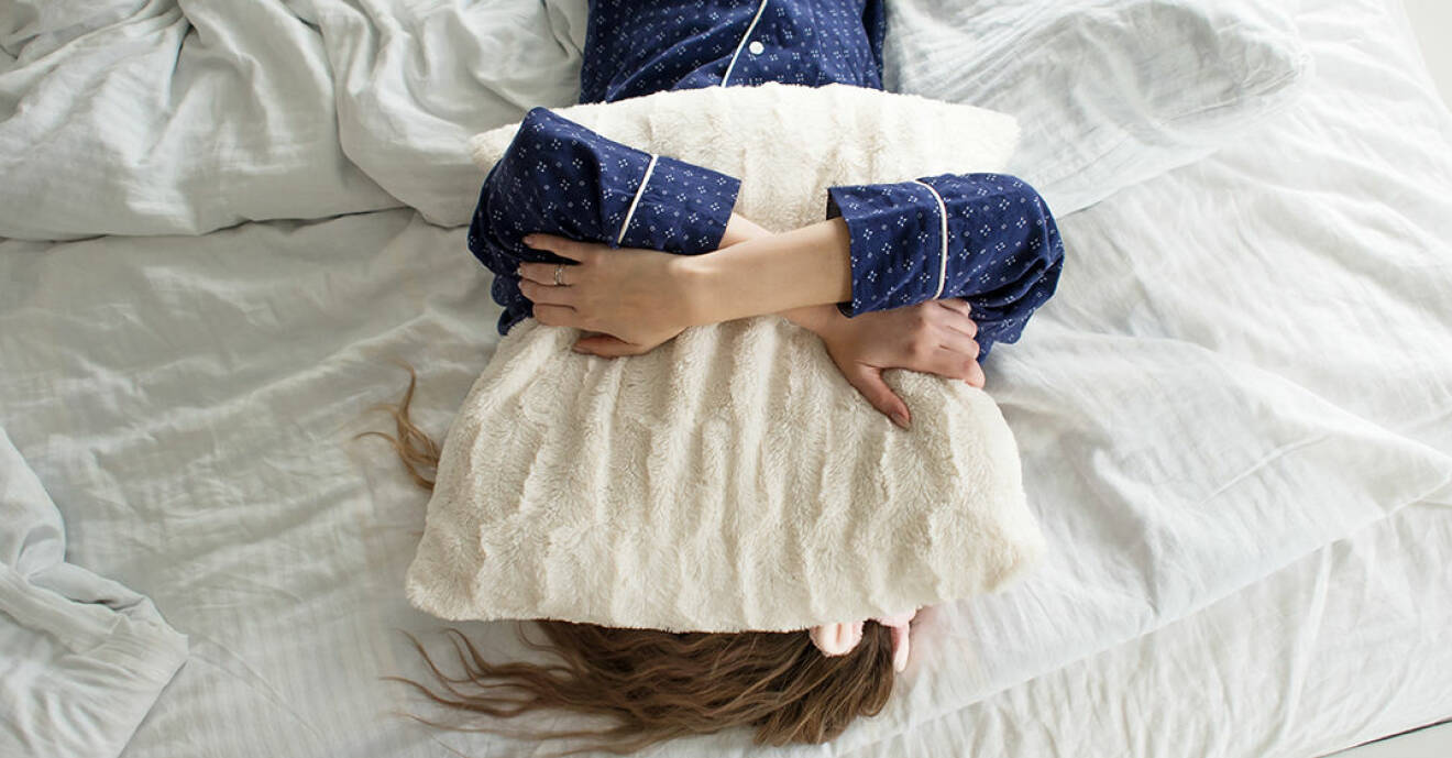 Kvinna med långt hår ligger på säng med kudde över huvudet