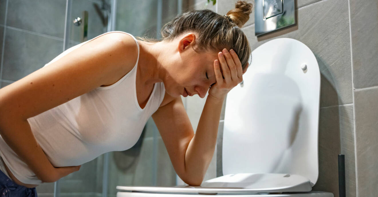 Illamående kvinna hukar över toastolen för att kräkas