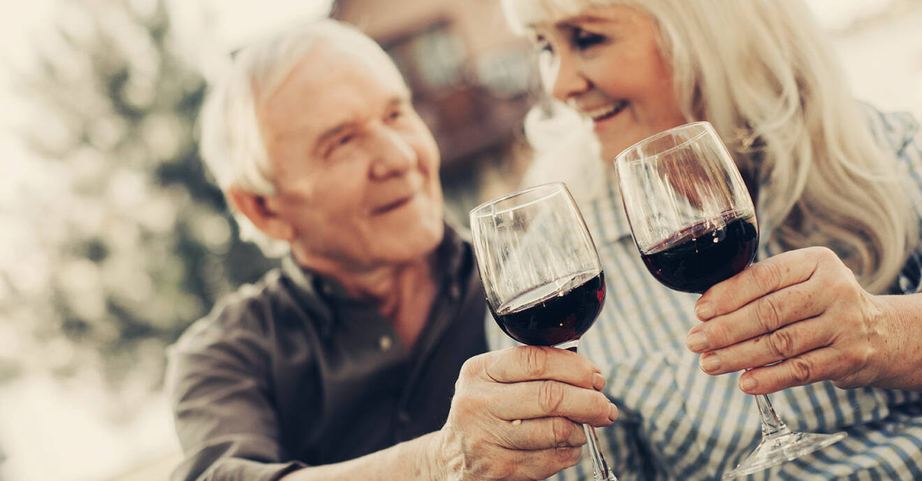 Äldre man och äldre kvinna sitter utomhus och skålar i rödvin.
