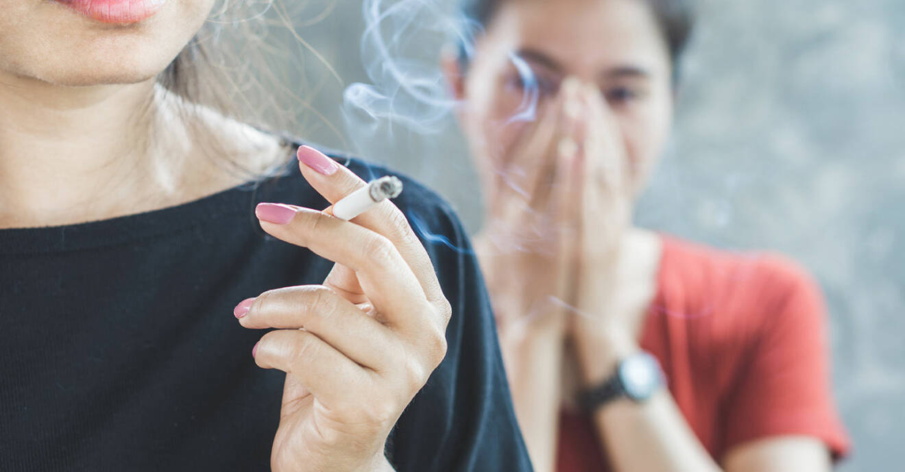Kvinna i förgrunden röker och en annan kvinna bakom henne håller för näsan.