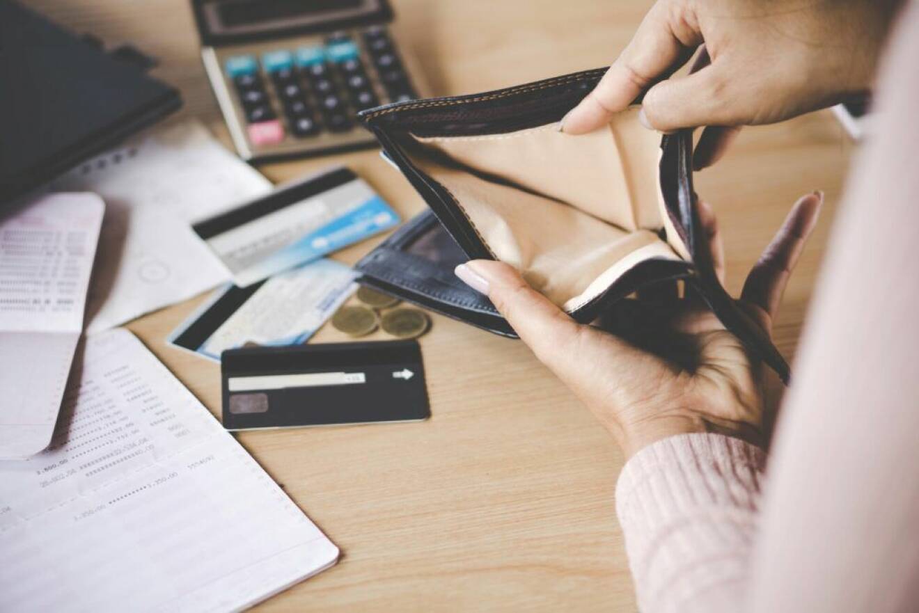 Kvinna som håller upp tom plånbok framför dator