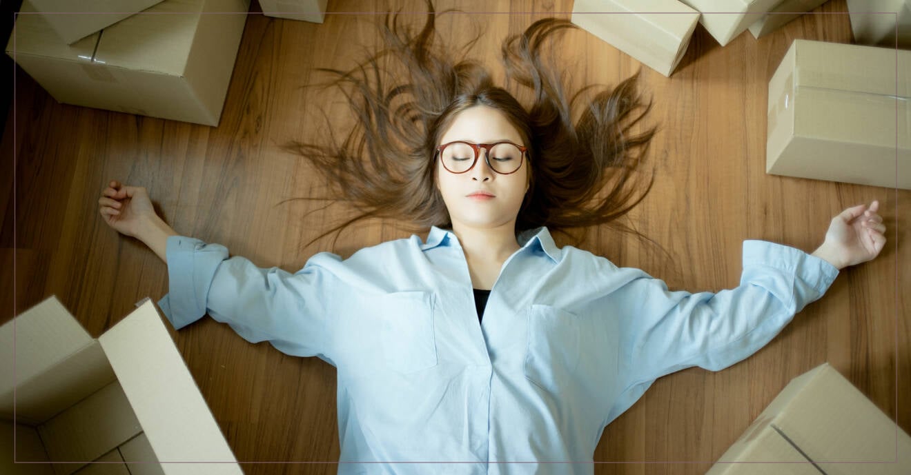 Ung kvinna ligger och blundar på golvet med kartonger runtomkring sig