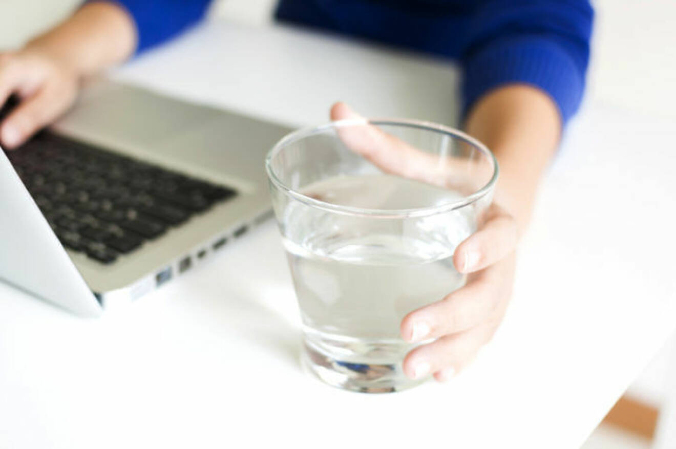glas med vatten på skrivbord vid dator