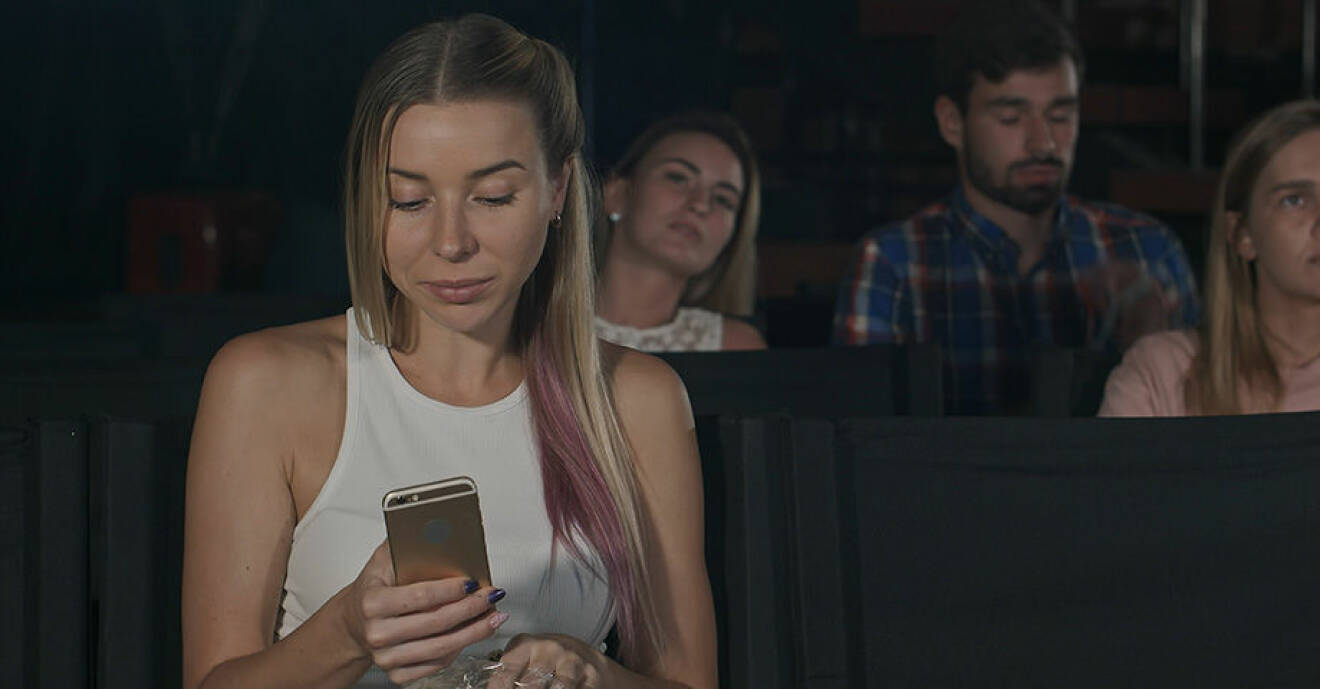 Kvinna kollar sin mobiltelefon när hon ser på bio.