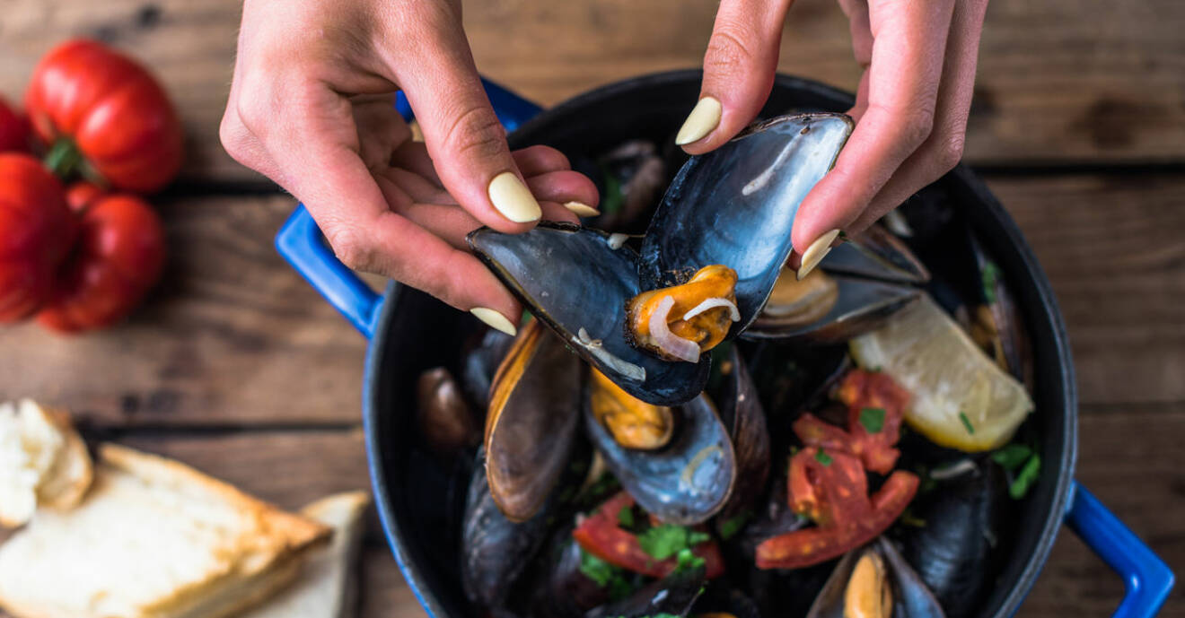 Kvinnohänder plockar upp musslor i skal ur blå kastrull