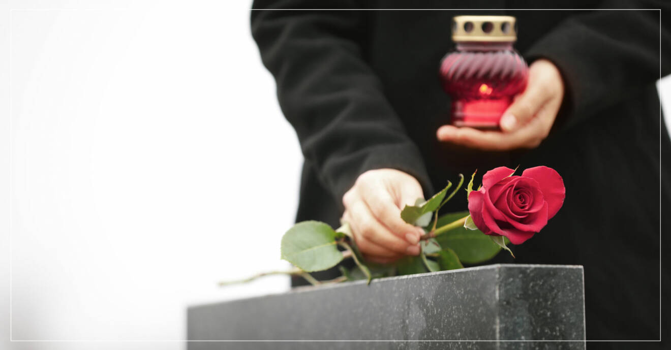 Sörjande kvinna lägger röd ros på gravsten och håller ljus i handen.