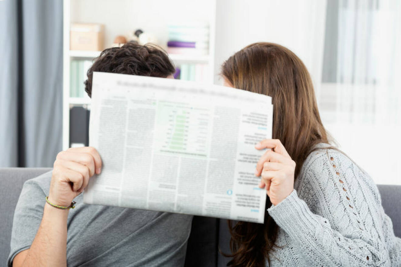 Young couple hiding behind newspaper