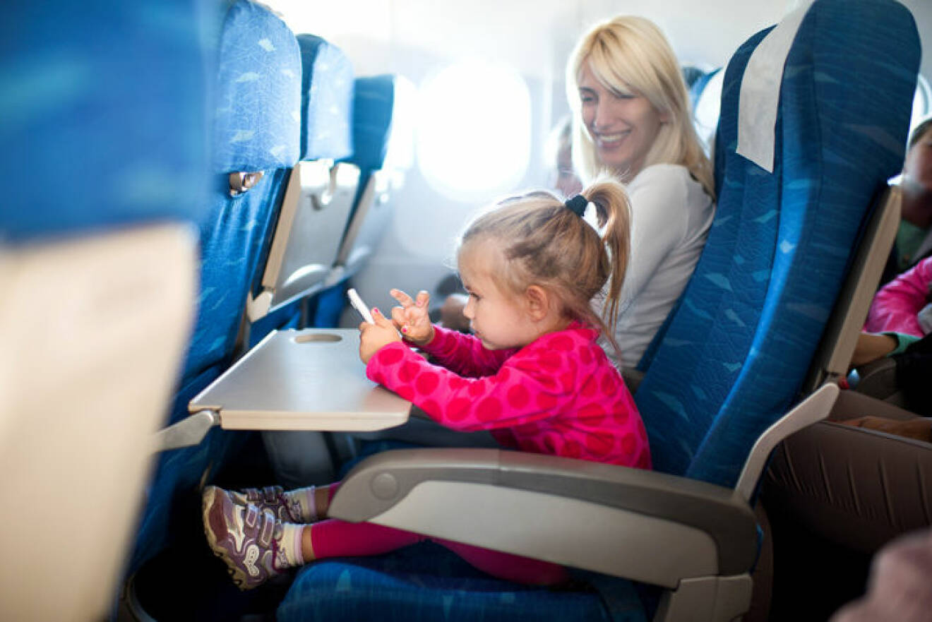 Little girl traveling by airplane with her mother and playing games on mobile phone. Focus is on foreground.