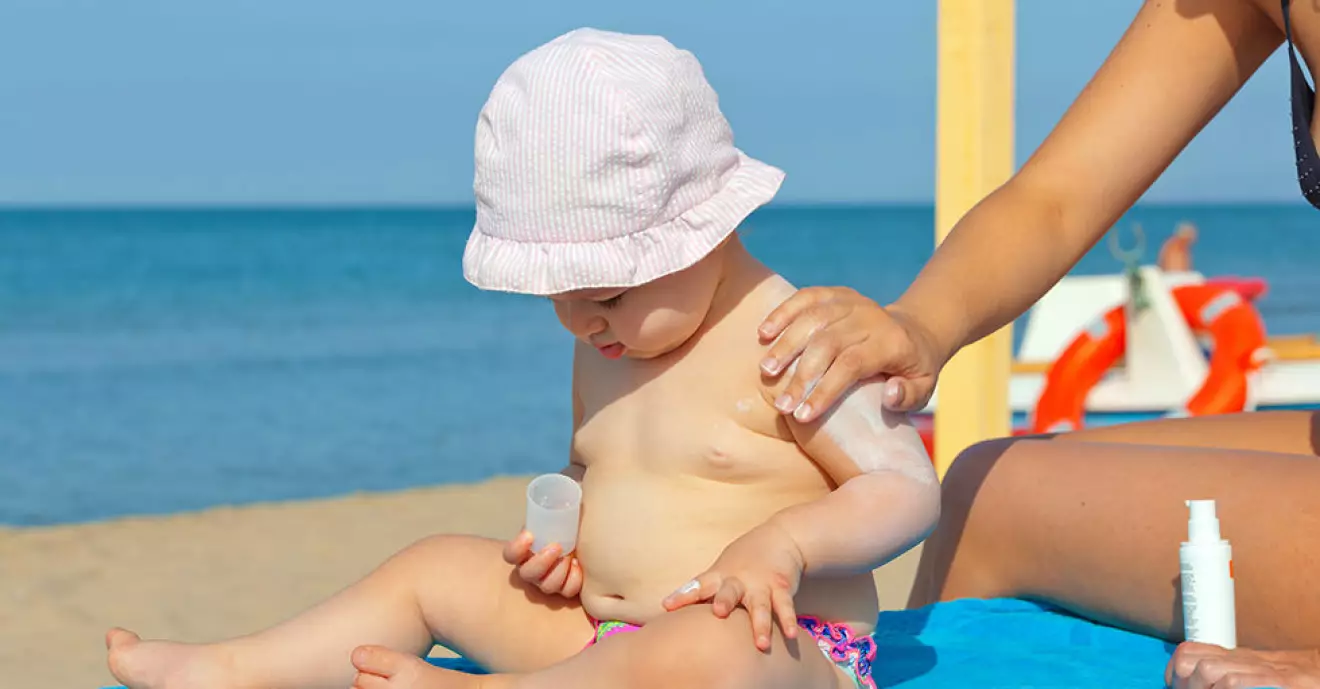 Mom puts sunscreen on the shoulders of her one year old daughter.