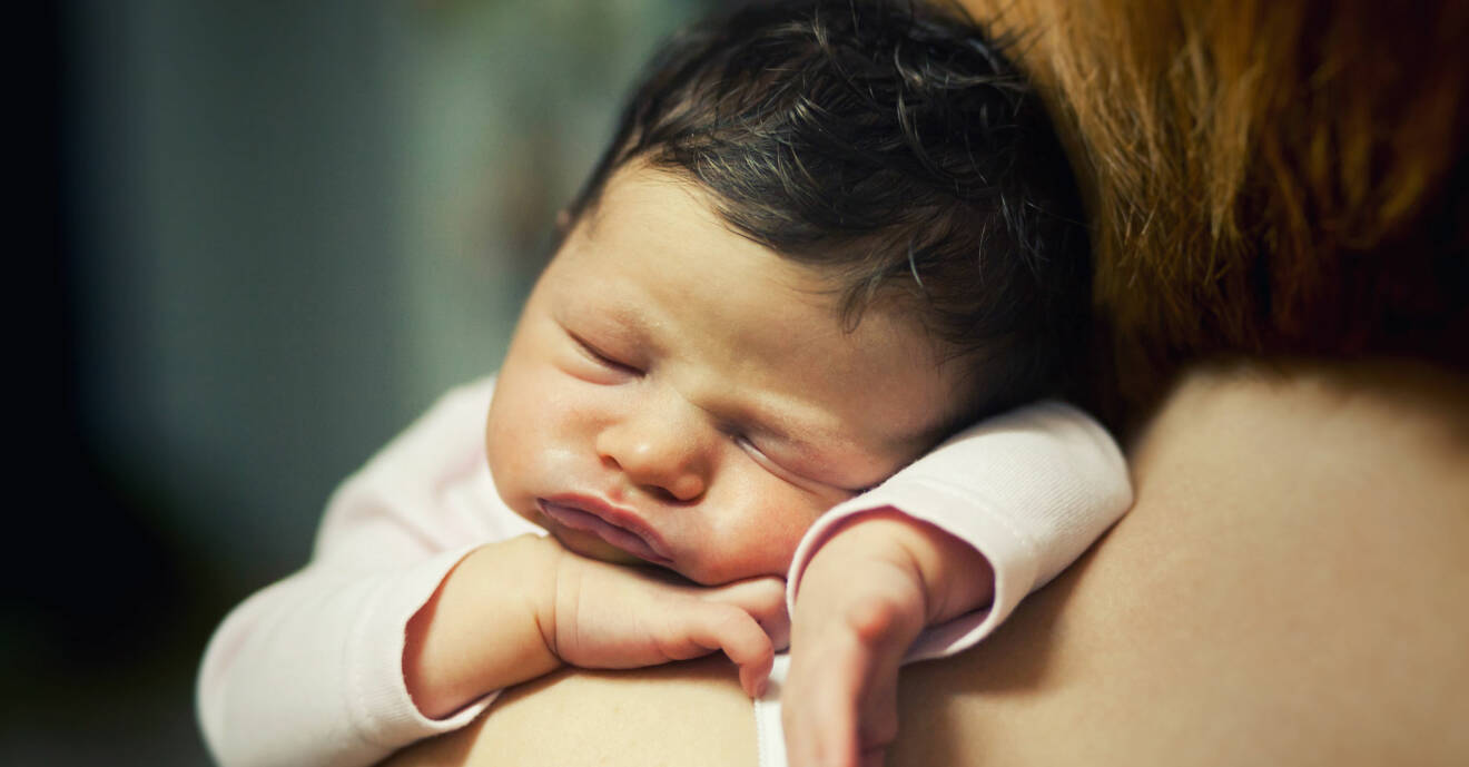 Trött bebis sover på sin mammas skuldra med trutande läppar