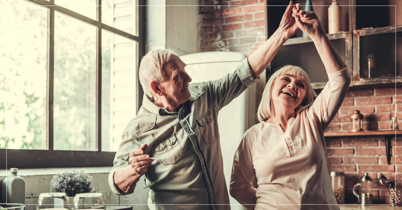 En äldre man och kvinna dansar tillsammans i köket