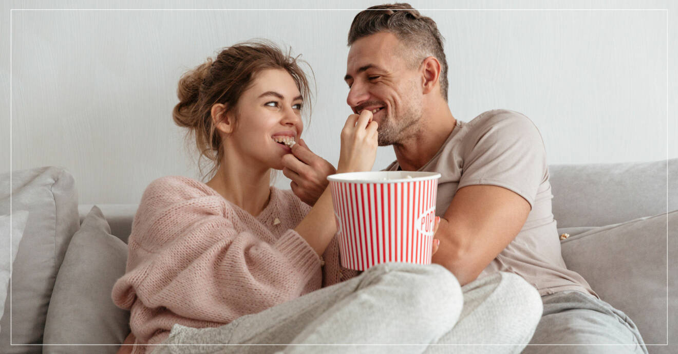 Par äter popcorn i soffan.